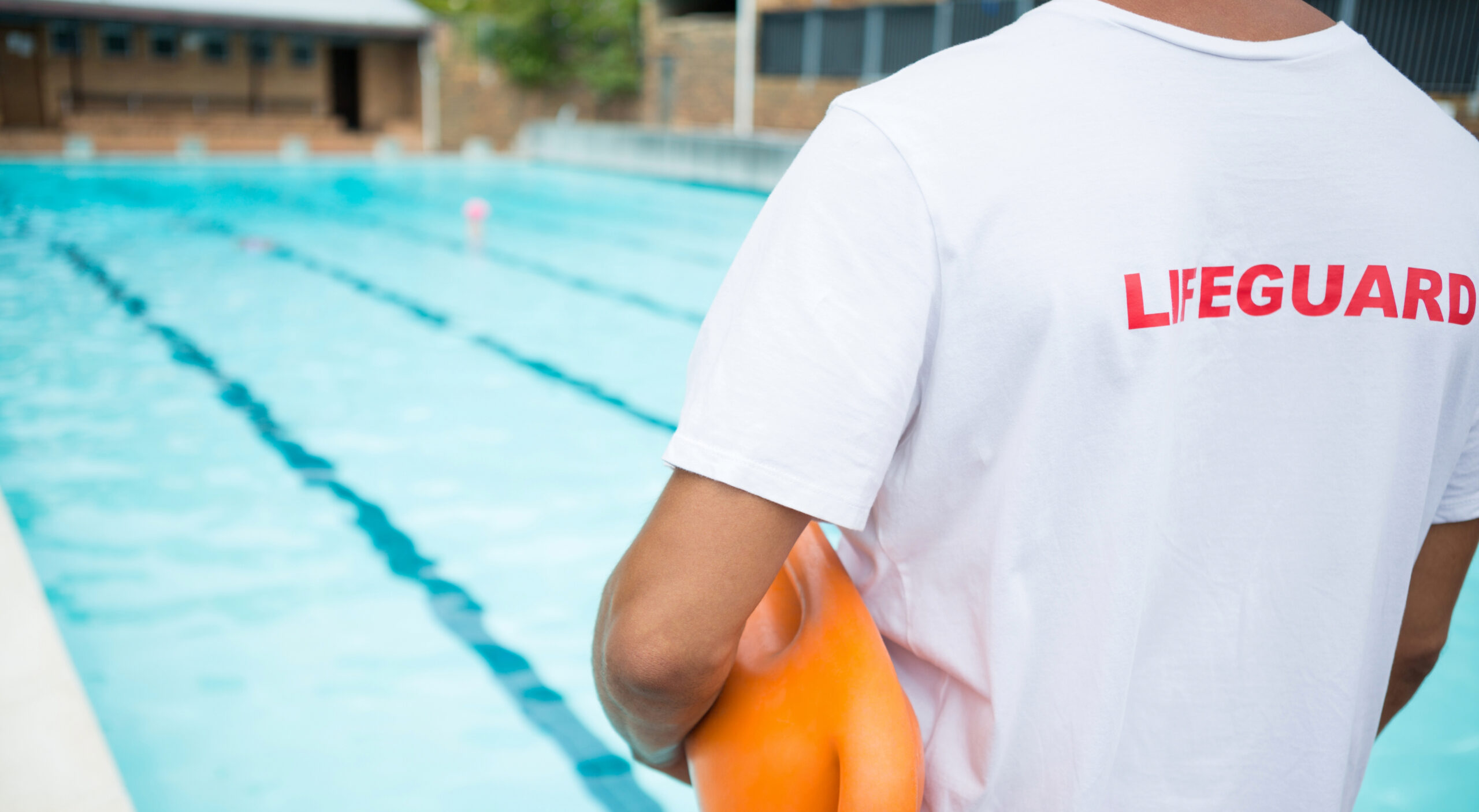 Lifeguard standing with rescue buoy poolside