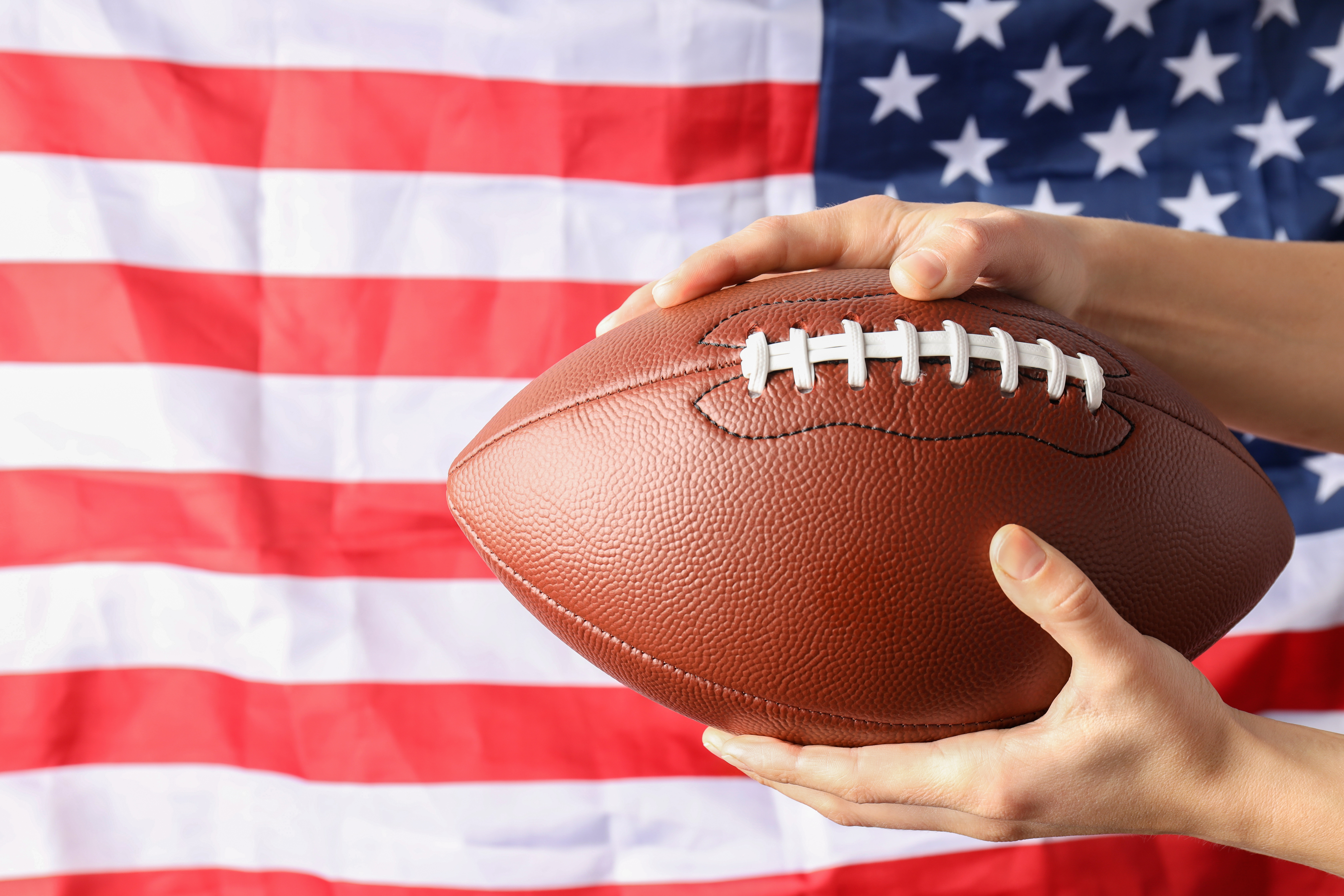 Super Bowl watch parties in Franklin and Nashville, TN, list of sports bars, restaurants and family entertainment centers showing the big football game_Football in hands with the US flag as background.