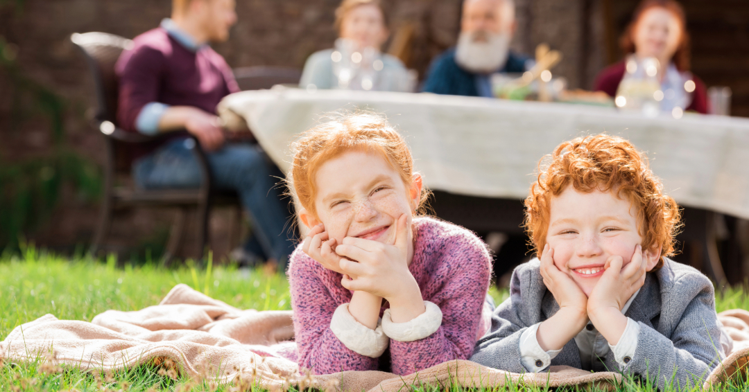 Children on picnic blanket with family int he background.