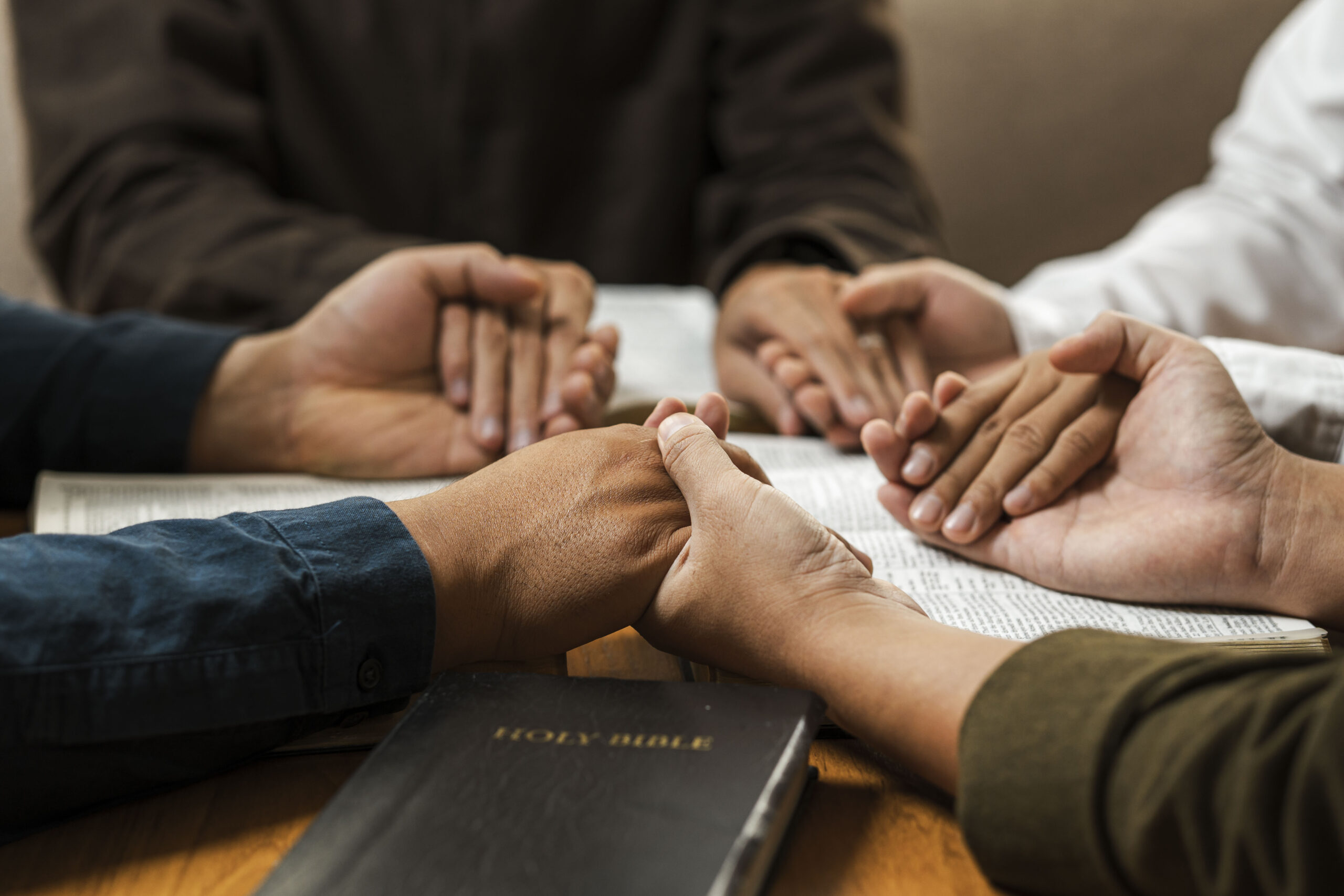 Four sets of hands together in prayer over a bible.