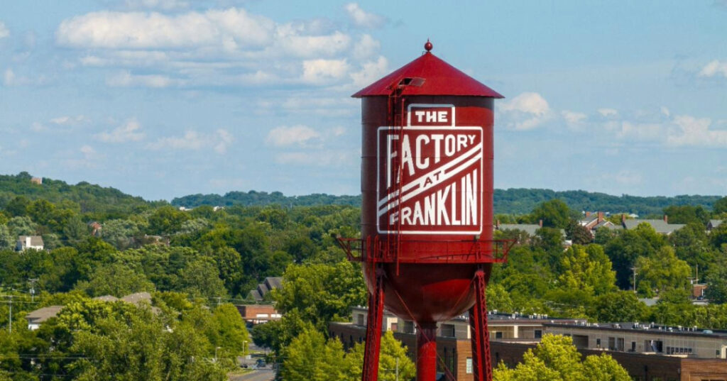 Iconic red water tower with The Factory at Franklin logo against a treetop skyline