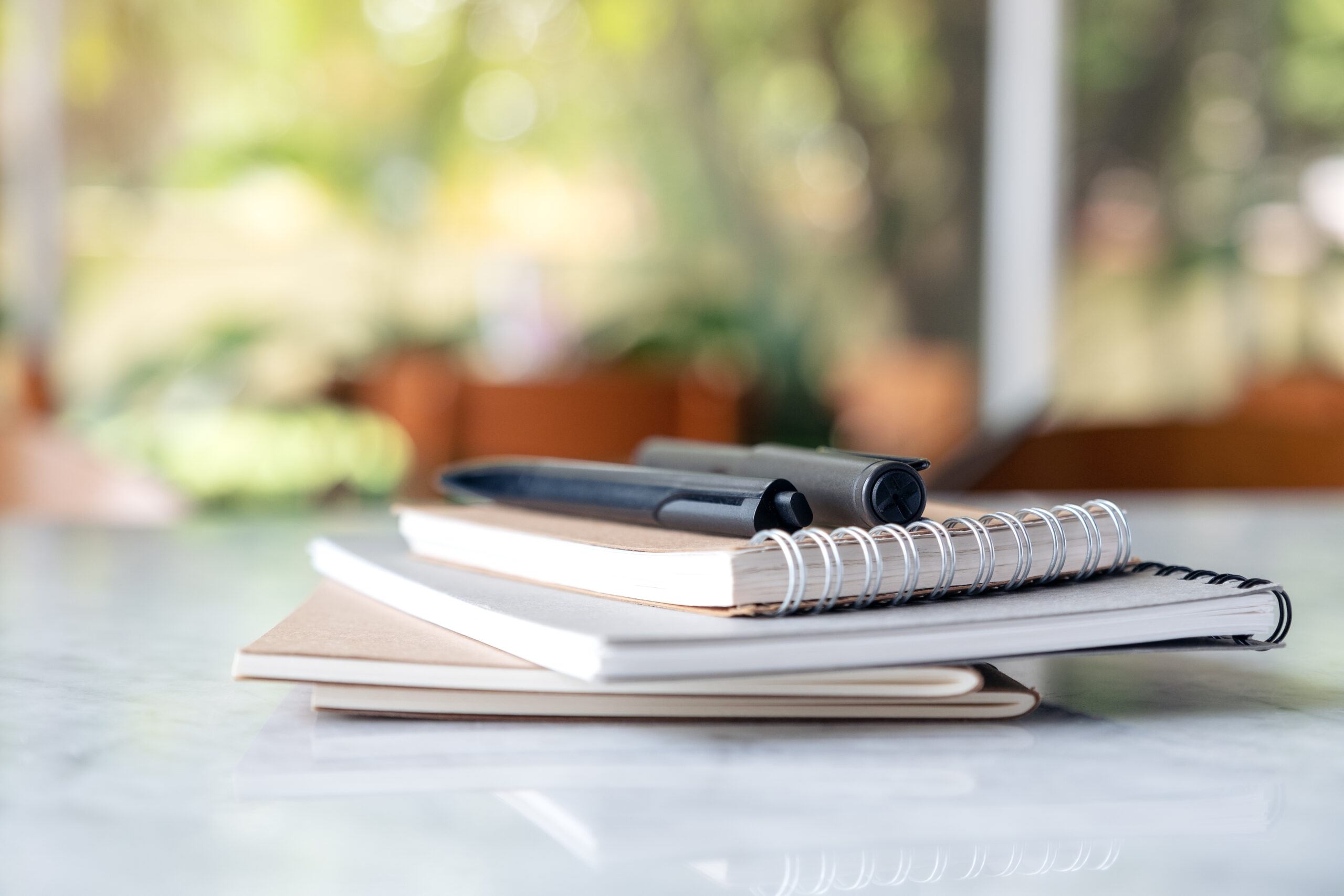 Books and notebooks with pens on the table with blur green nature background.