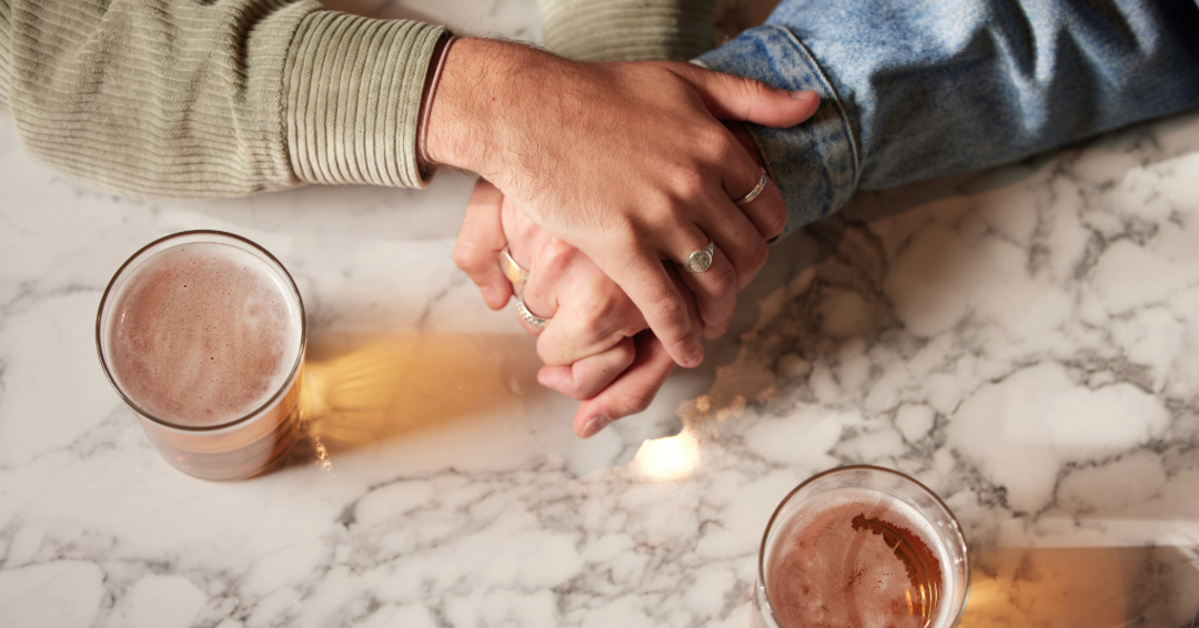 A couple holding hands over a table, with beverages on it