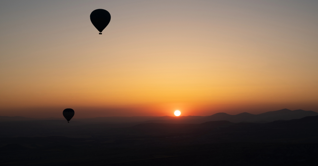 Hot Air Balloons float over mountains at sunrise.