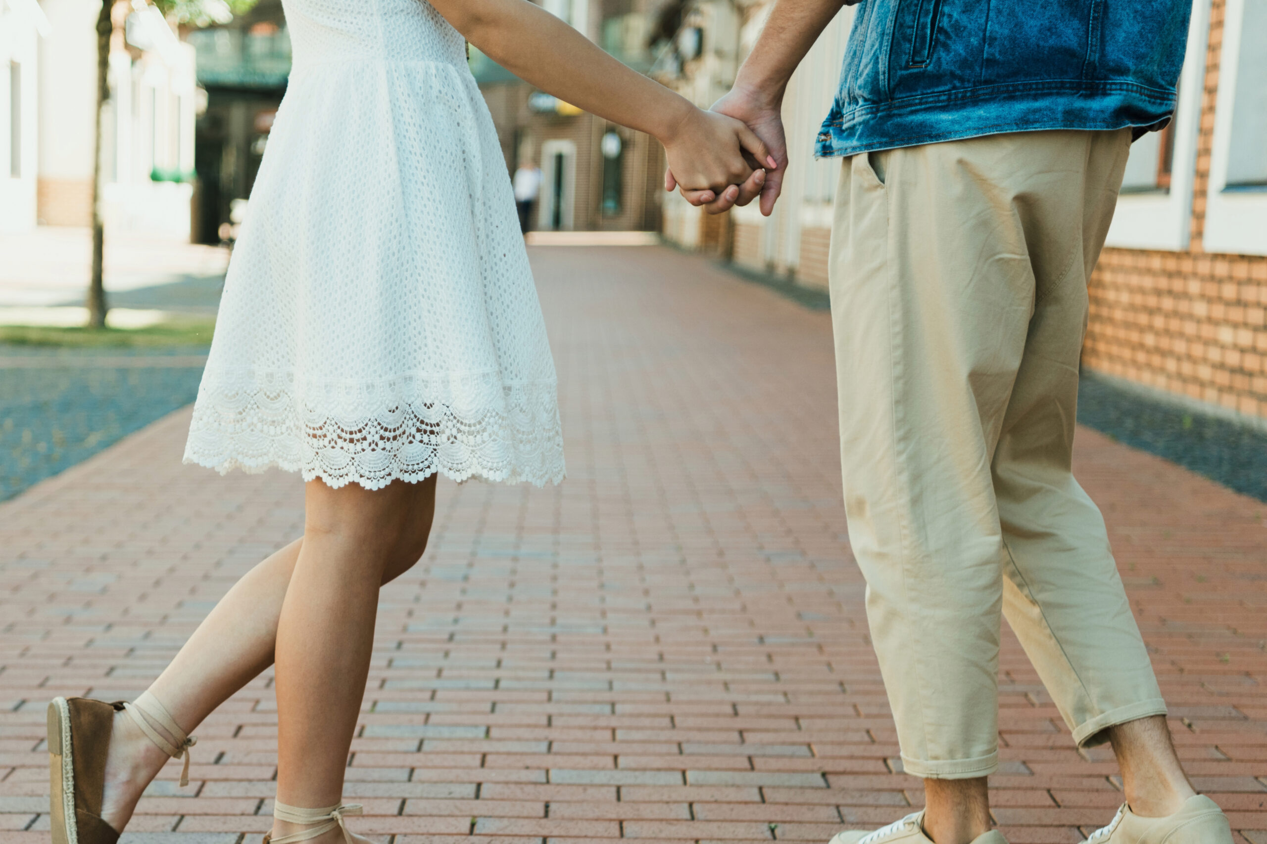 A couple on a brick sidewalk facing one another, holding hands.