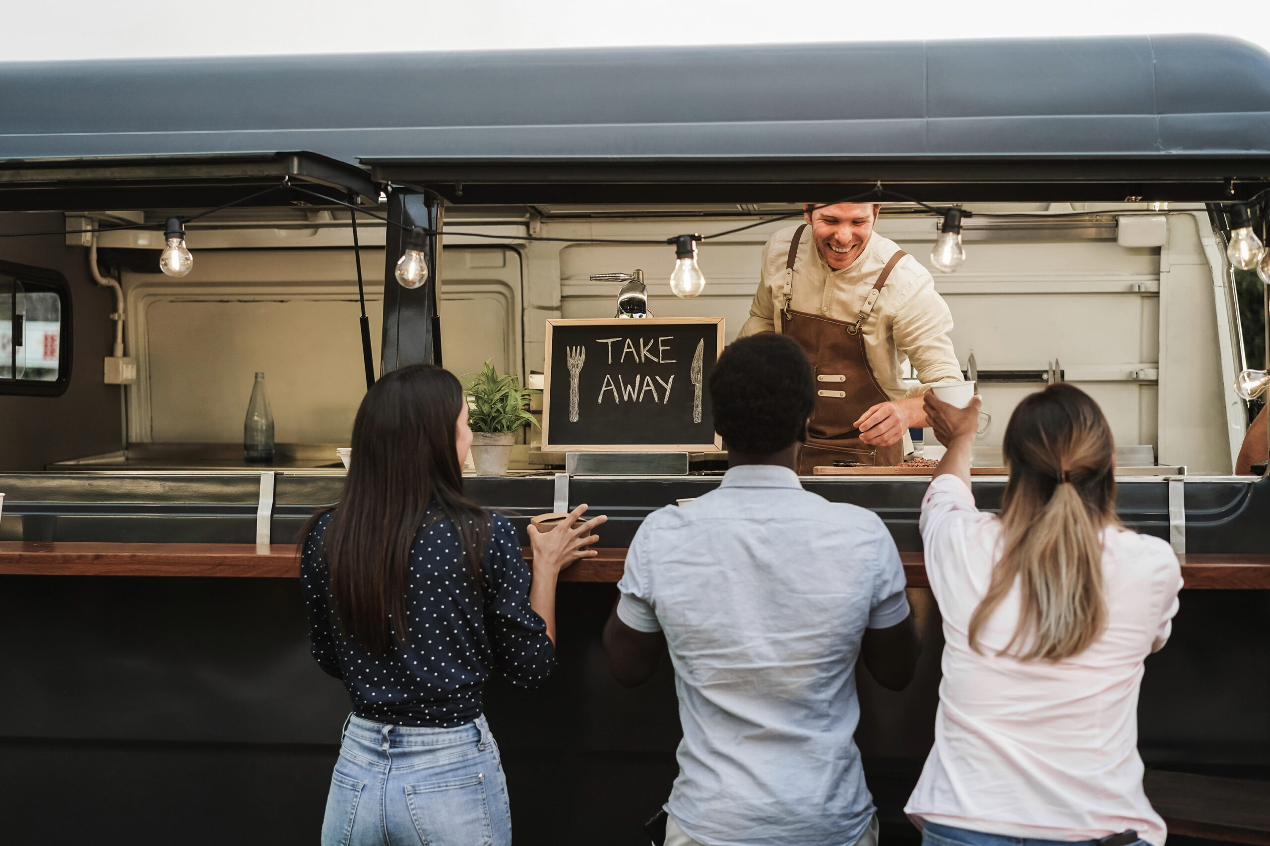 Three people are ordering at the window of a food truck.