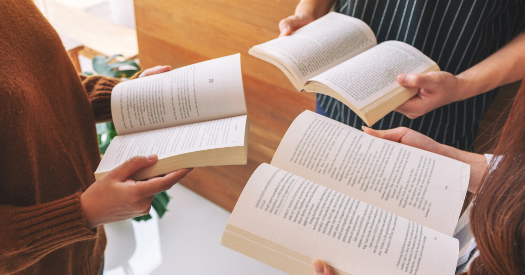 A group of 3 people gathered with books open 