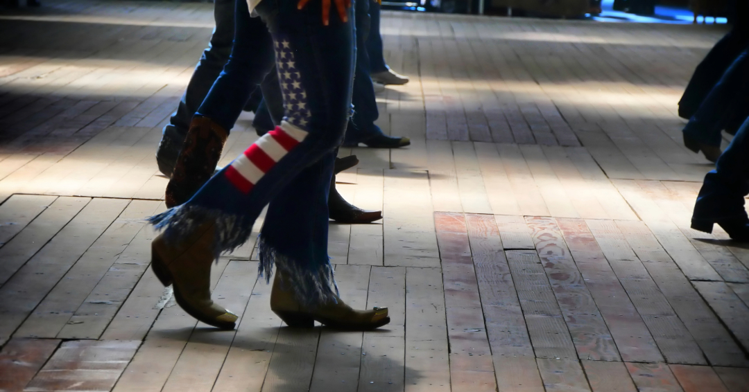 A woman line dancing, wearing cowboy boots and jeans with American Flag details.