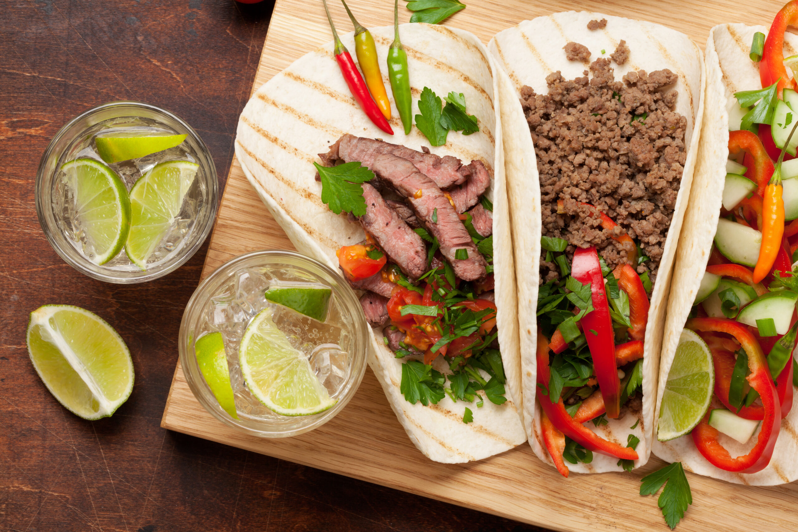 Set of mexican tacos with meat and vegetables in tortilla. And caipirinha cocktail. Top view on wooden table. Flat lay