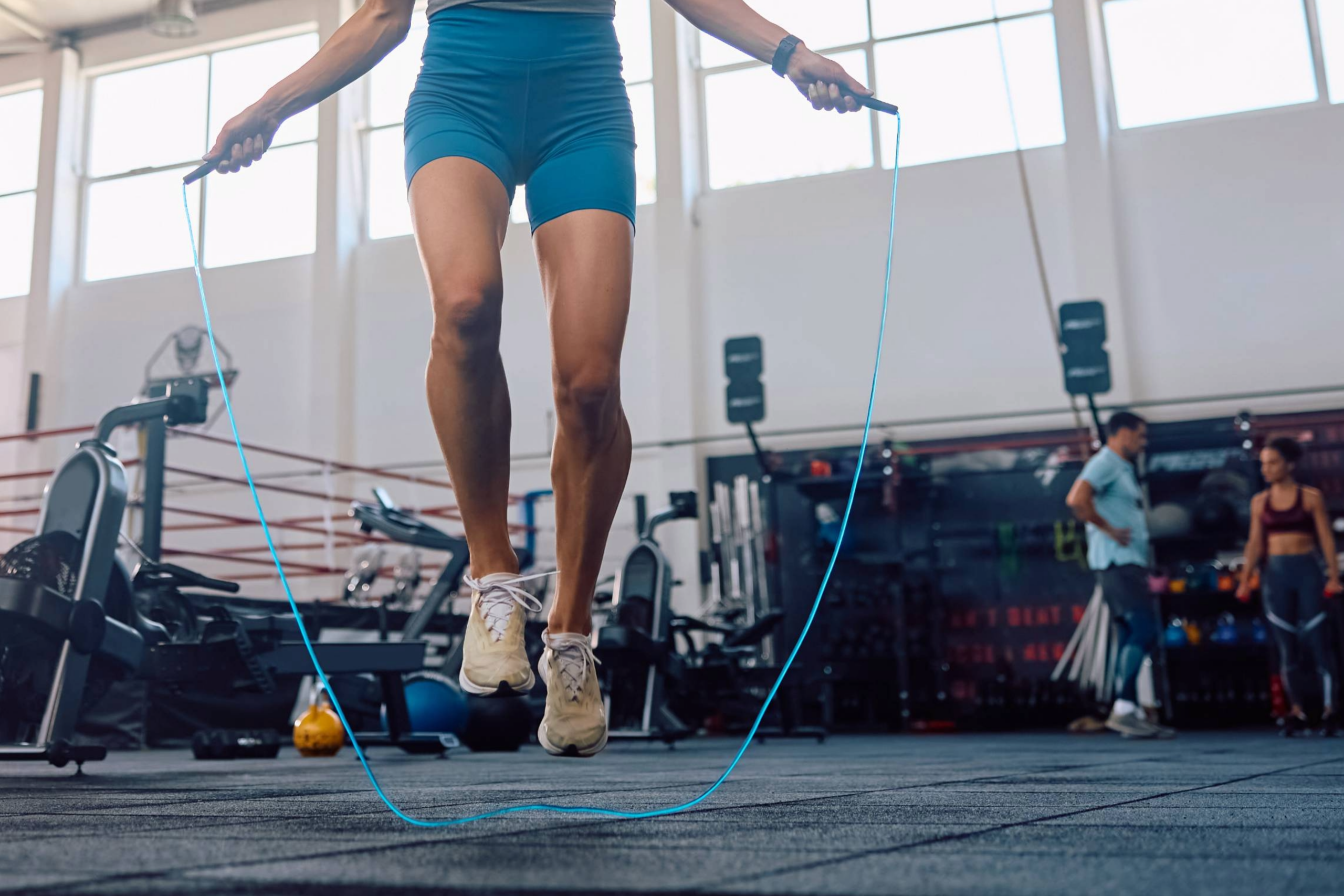 An athletic woman in a Franklin, TN gym uses a jump rope. Behind her is a boxing ring, exercise equipment, and other people workout out.