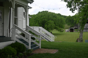 Side porch of Hayes House with string lights, barn and rolling pasture in background