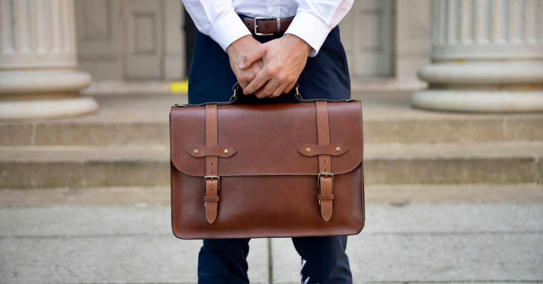 Men’s accessories in Franklin and Brentwood, TN, featuring a classic brown leather briefcase held by a man in a white shirt and navy pants.