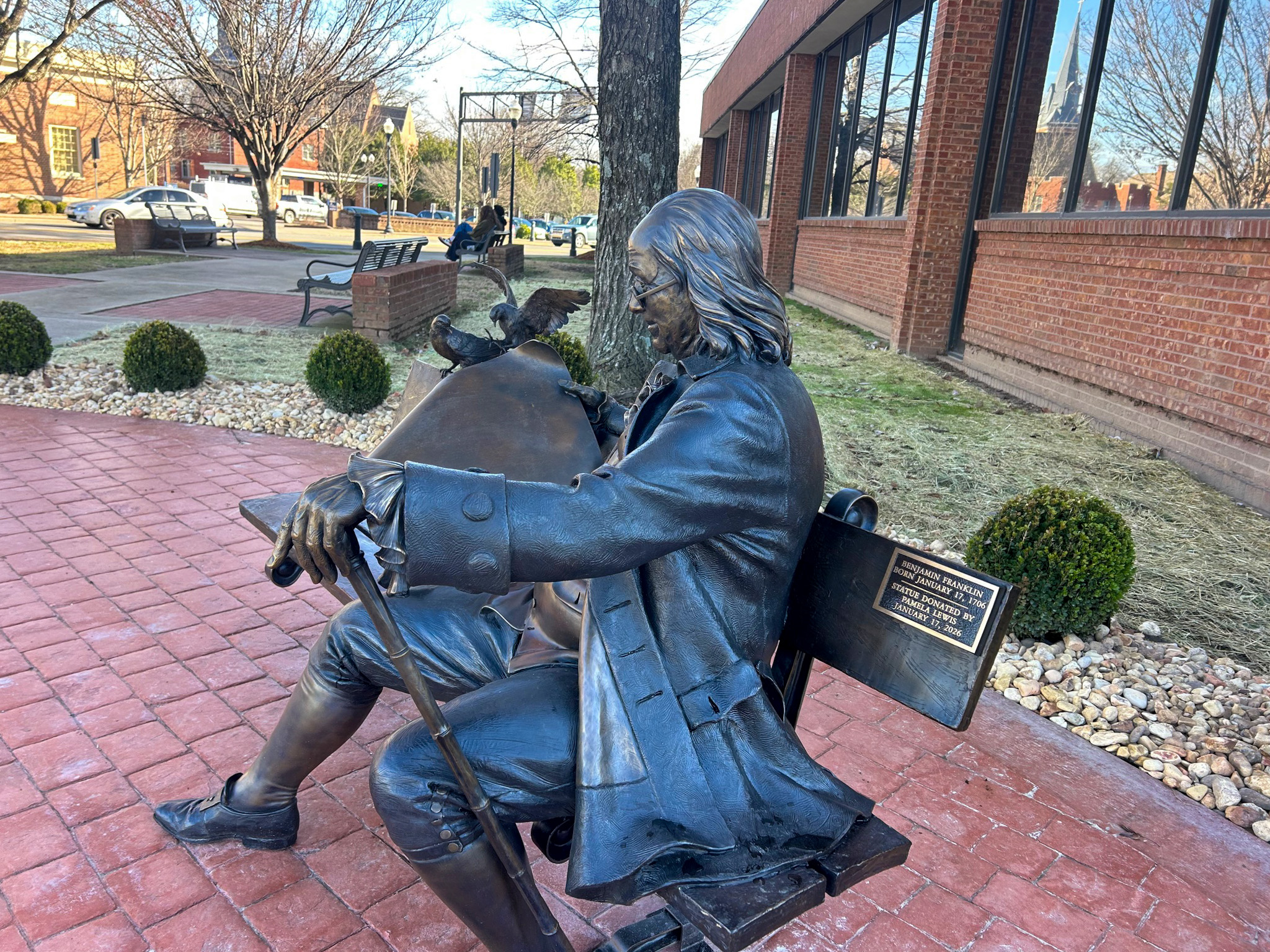 Ben on the Bench statue in downtown Franklin, Tennessee, shown from a side angle with Benjamin Franklin seated reading a document beside the Williamson County Archives and Museum.