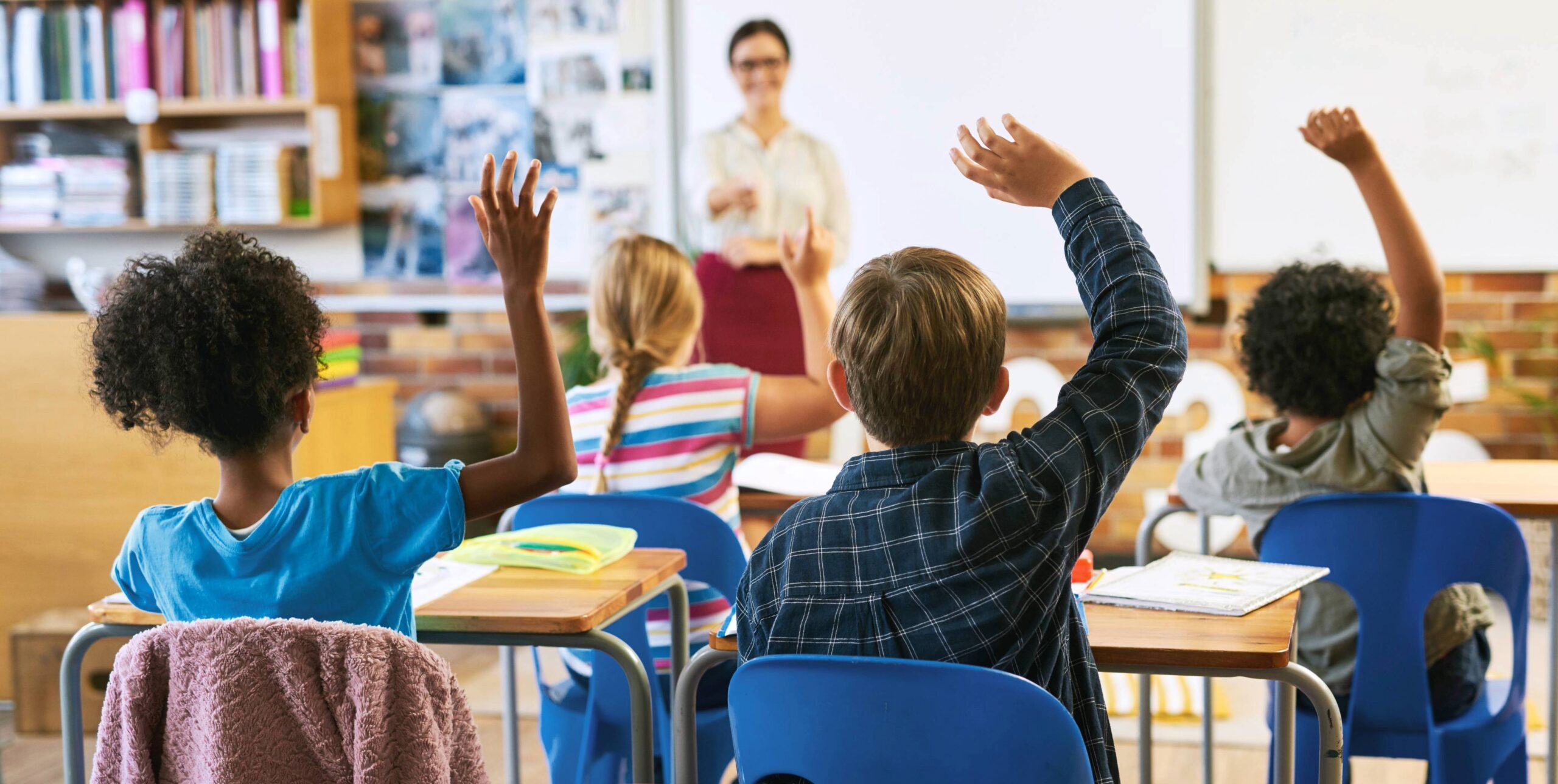 Organizations removing barriers to learning for children in Williamson County, TN, shown through students participating in a classroom lesson with hands raised and engaged in learning.