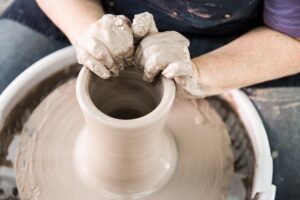 At The Clay Lady's Campus in Nashville, TN, a student in a pottery workshop is making a piece of clay on a pottery wheel.