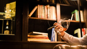 Cigar lounges, bars, and shops Franklin, TN, man with a glass of whiskey and a cigar, and bookshelves in background.
