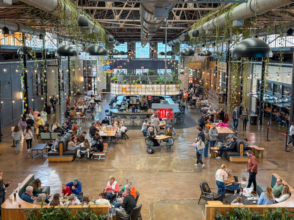 Bustling Grand Hall at The Factory at Franklin with Skylight Bar, hanging plants, diners, and industrial ceiling beams