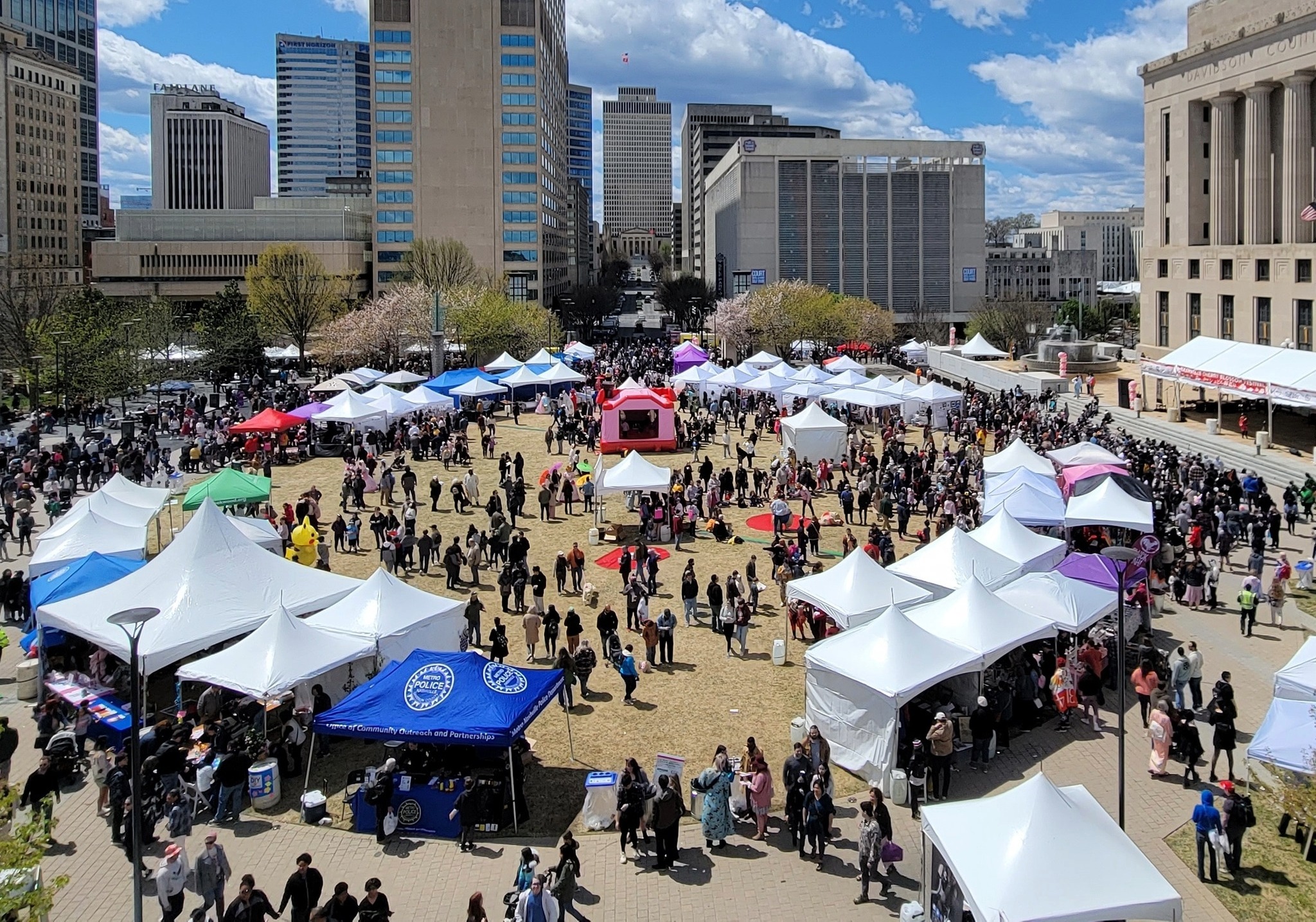 Crowds and vendor tents at the Nashville Cherry Blossom Festival in Public Square Park with downtown Nashville skyline
