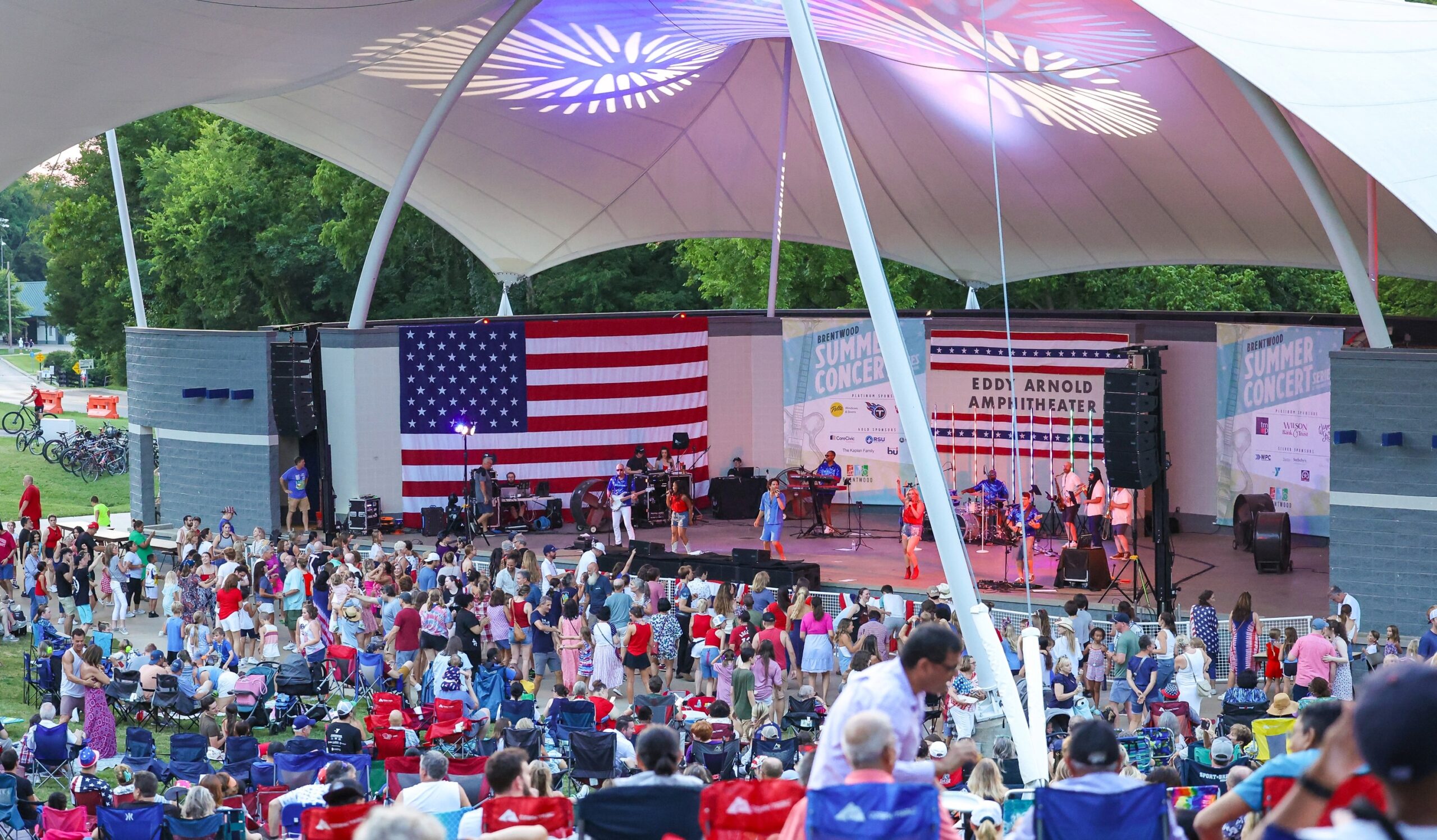 Crowd gathered at the Eddy Arnold Amphitheater in Crockett Park for Brentwood’s Red, White, and Boom! celebration, with a live band performing in front of a large American flag.
