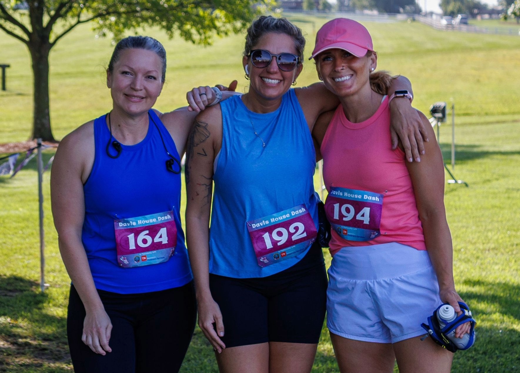 Three participants pose together at the Davis House Dash Fun Run in Franklin, Tennessee, wearing race bibs and athletic clothing on a grassy field.