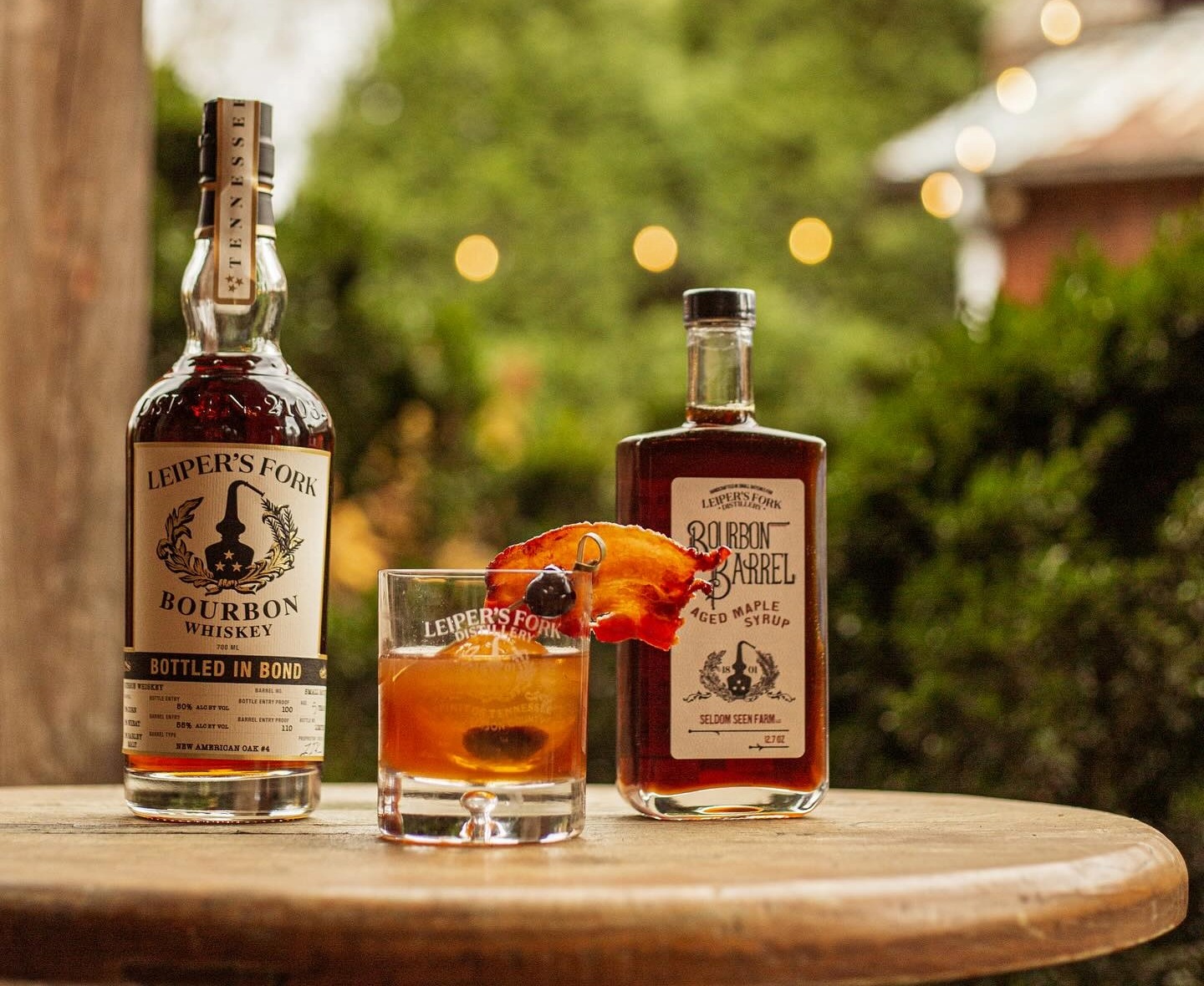 Leiper's Fork Distillery Nashville bourbon whiskey bottle, cocktail, and bourbon barrel-aged maple syrup displayed outdoors