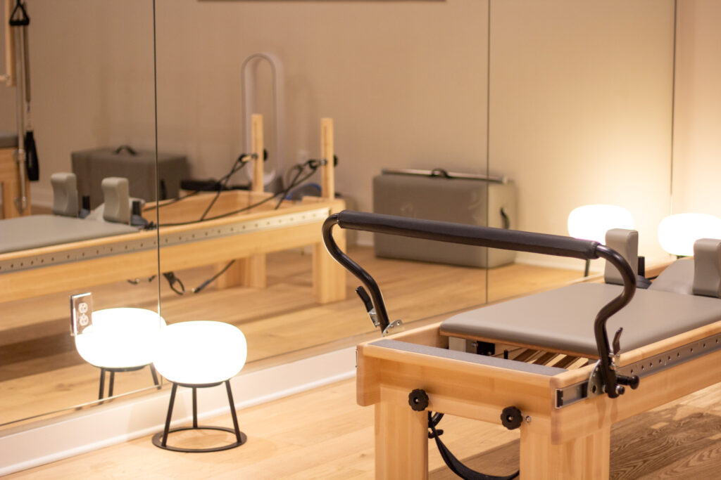 Pilates reformer equipment positioned beside large mirrors with warm studio lighting at Pendulum Pilates and Wellness in The Factory at Franklin, TN