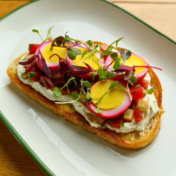 Truce Brentwood TN Toast Menu Item Truce Brentwood TN. showing toast topped with creamy spread, chopped vegetables, sliced eggs, and microgreens on a white plate.