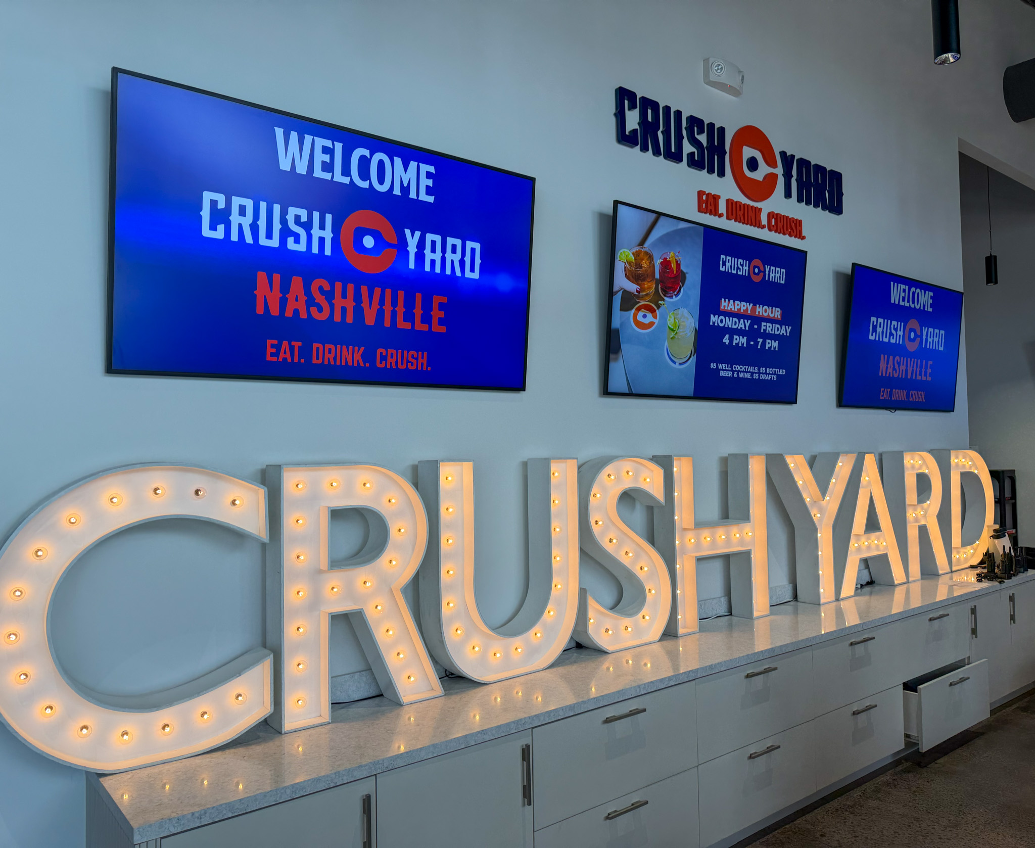 Crush Yard Nashville signage inside the Brentwood, TN, entertainment venue, with welcome screens, happy hour information, and lighted Crush Yard letters.
