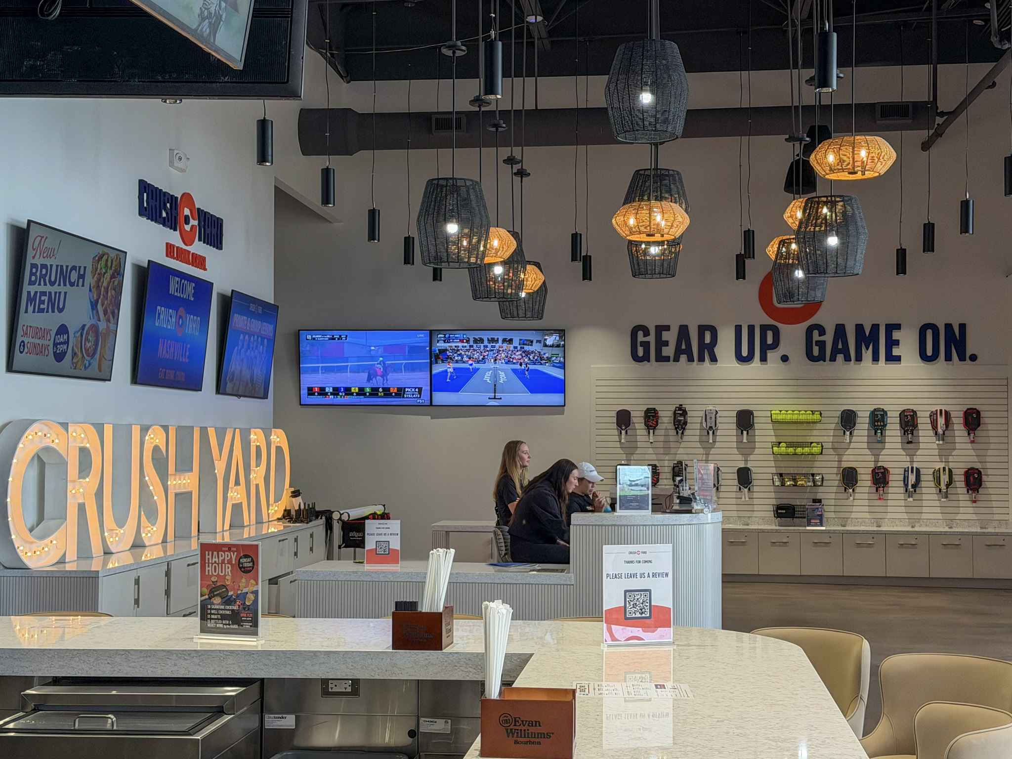 Interior of Crush Yard Nashville in Brentwood, TN, showing the sports bar and lounge area, pickleball gear wall, TV screens, and Crush Yard signage.
