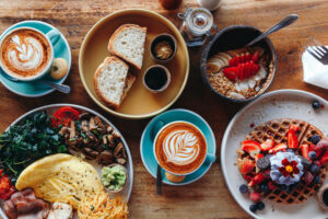 Healthy morning breakfast spread on a table featuring waffles with cream and berries, coffee and cappuccino, vegetable omelet, bread with butter, avocado cream, and fresh vegan food options.