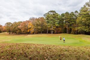 Golfers on a green at Montgomery Bell State Park Golf Course in Tennessee surrounded by wooded fall scenery.