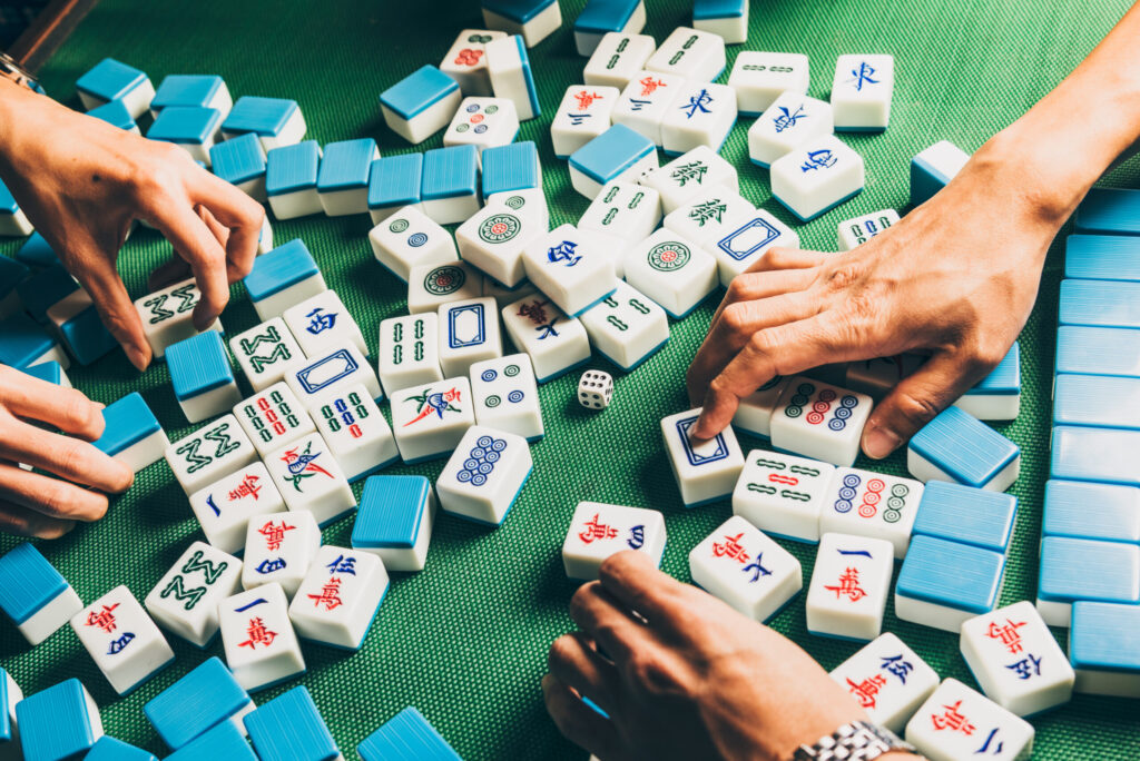 Four people playing Mahjong with blue and white tiles on a green game table