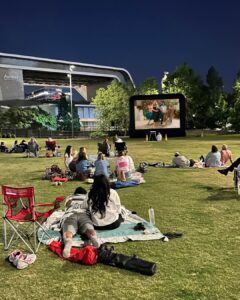 People watching an outdoor movie on the lawn at Riverfront Park in downtown Nashville, Tennessee, with Ascend Amphitheater in the background.