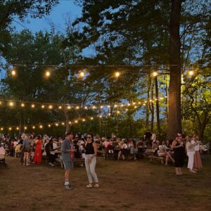Evening gathering at Shelby Park in Nashville with picnic tables, string lights, and visitors beneath mature trees.