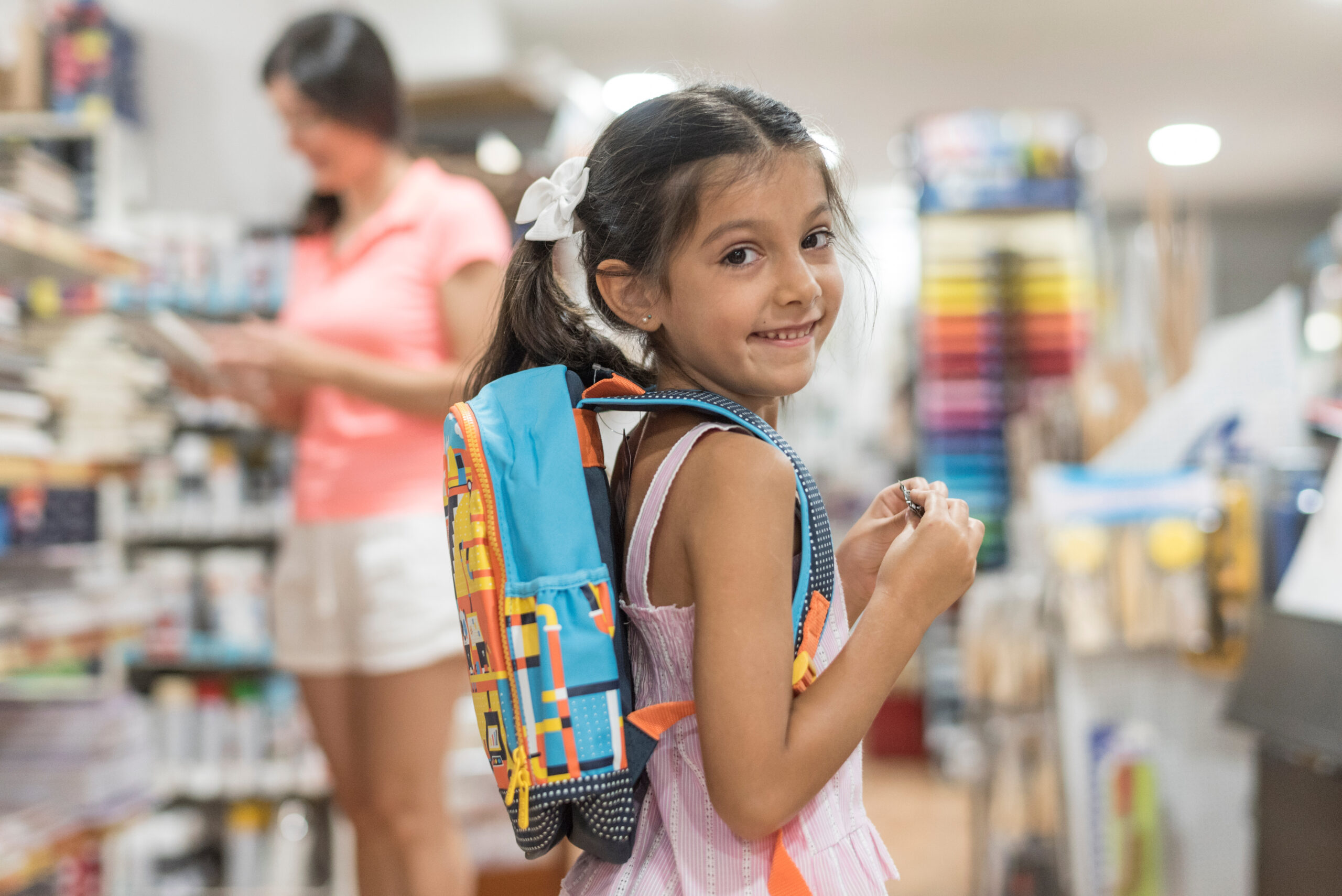 Young girl tries on a colorful backpack while shopping for school supplies during Tennessee’s back-to-school sales tax holiday.
