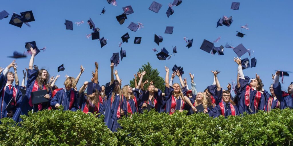 Thales Academy graduates celebrating outdoors by tossing their graduation caps into the air.