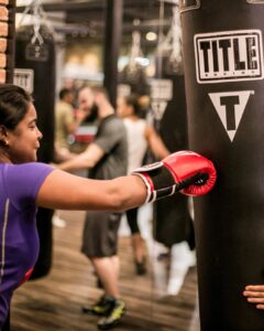 Woman wearing boxing gloves training on a heavy bag at TITLE Boxing Club in Franklin, Tennessee.