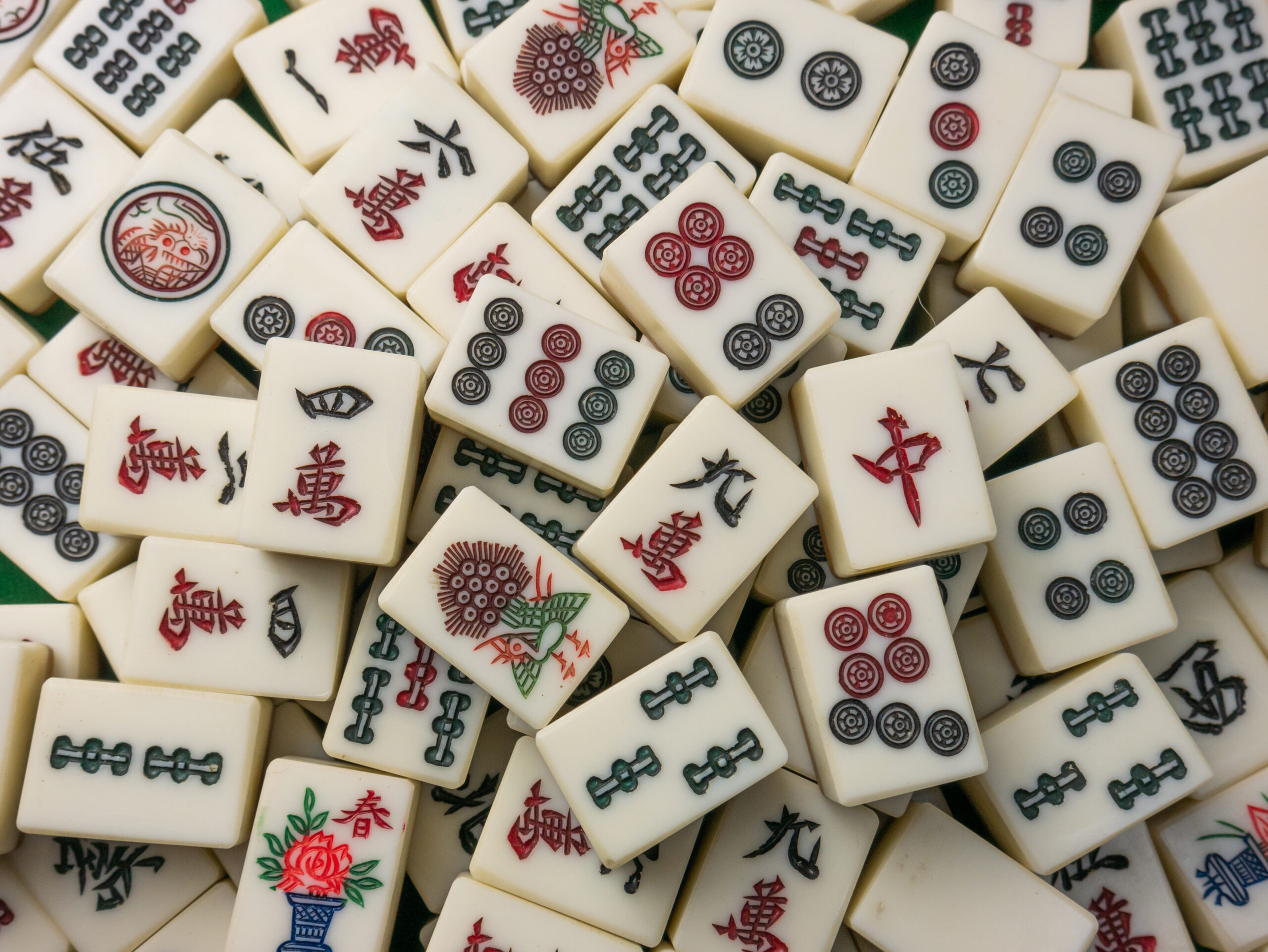 Mahjong - What to Know Before You Go, confirm if a beginner lesson, guided play, or open play before signing up. Close-up of assorted Mahjong tiles showing numbered suits, characters, flowers, and special symbols.