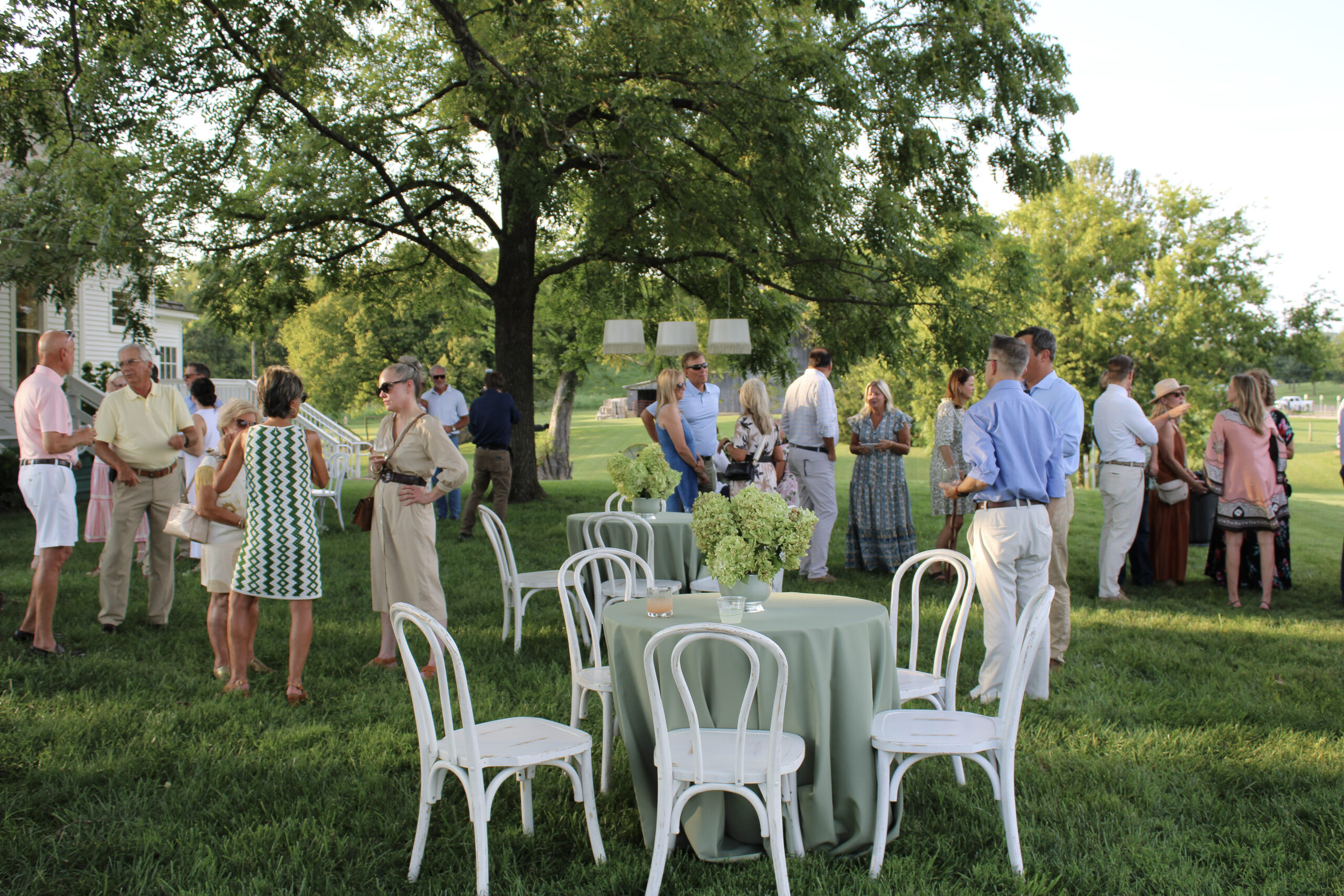 Guests gather beneath a large tree on the lawn at Hayes House during the 2026 Raise the Roofs Sponsors Party in Franklin, Tennessee.