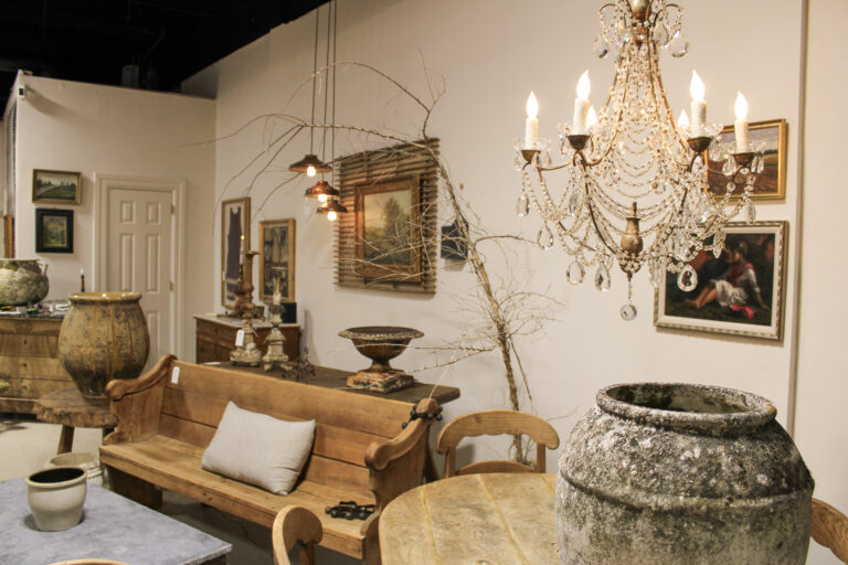 Crystal chandelier hanging above antique wooden furniture, rustic pottery, and framed artwork at the City Farmhouse warehouse showroom in Franklin, Tennessee.