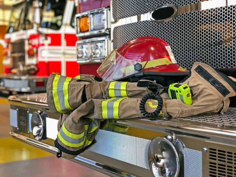 Firefighter helmet and protective turnout gear resting on the front bumper of a fire truck inside a fire station.