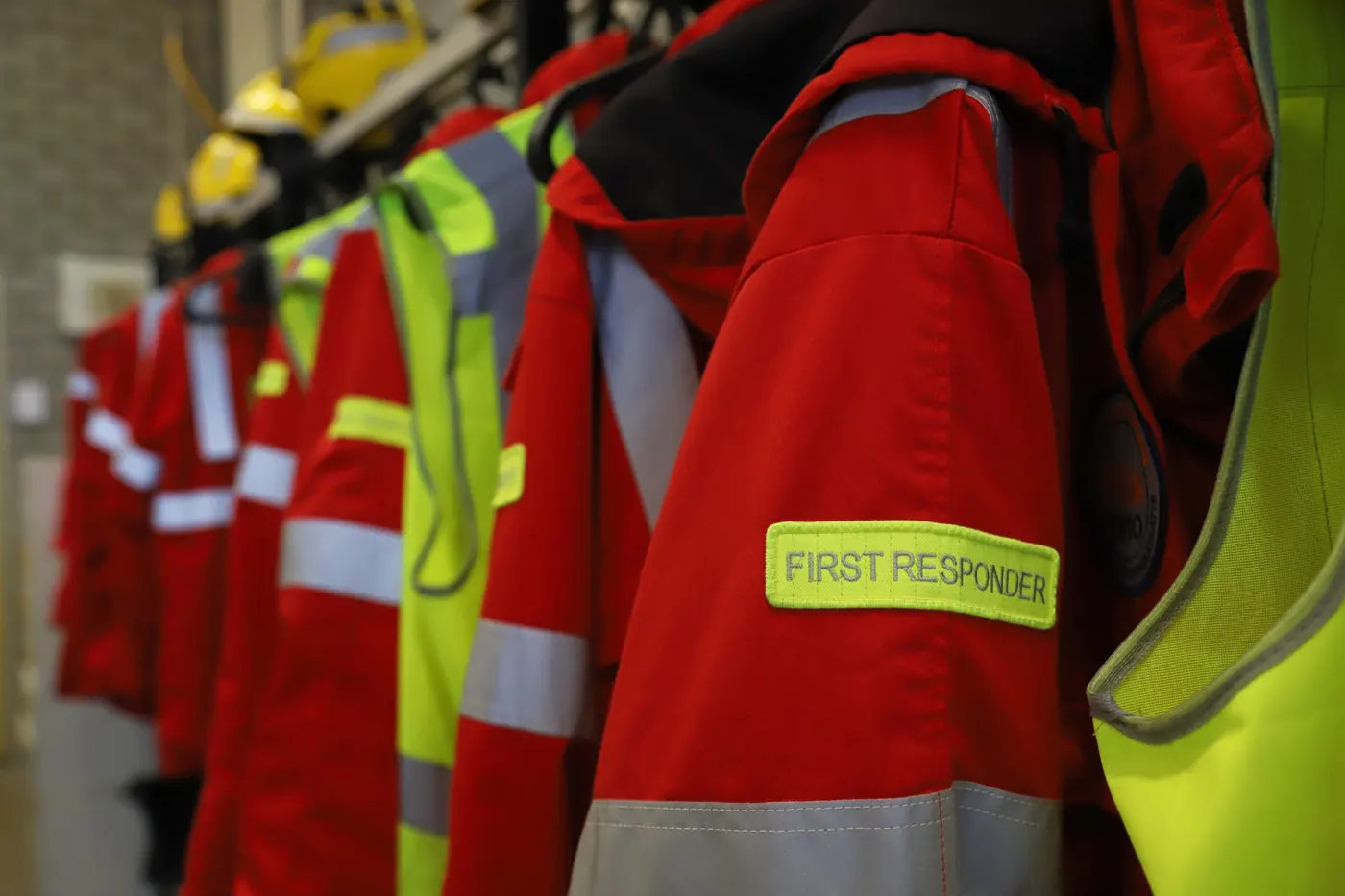 Red and high-visibility yellow first responder jackets hanging on hooks, including a uniform labeled First Responder.