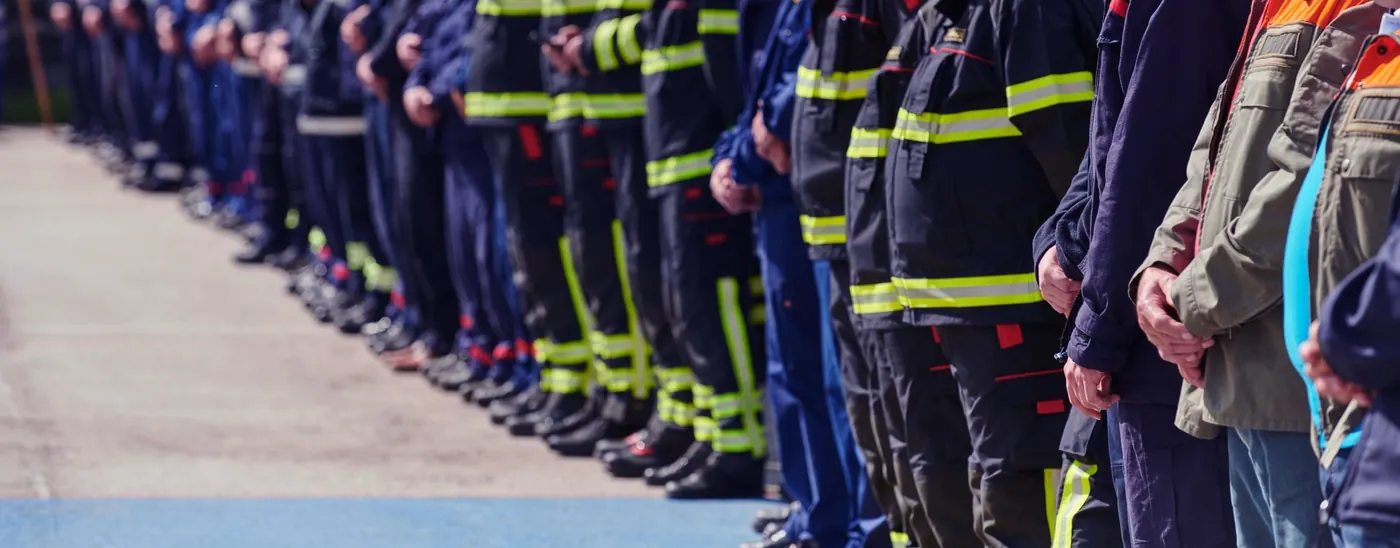 Line of firefighters and emergency responders standing together in uniforms with reflective yellow stripes.