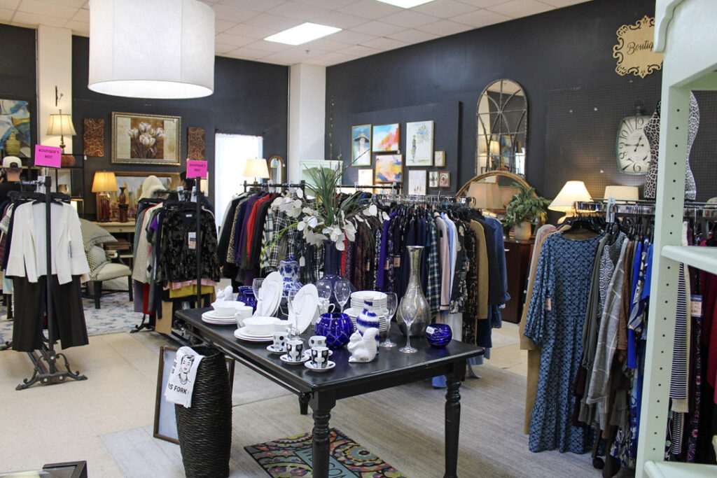 Racks of women's dresses, blouses, jackets, and sweaters arranged around home decor displays at GraceWorks Thrift in Franklin, TN.