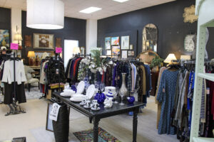 Racks of women's dresses, blouses, jackets, and sweaters arranged around home decor displays at GraceWorks Thrift in Franklin, TN.