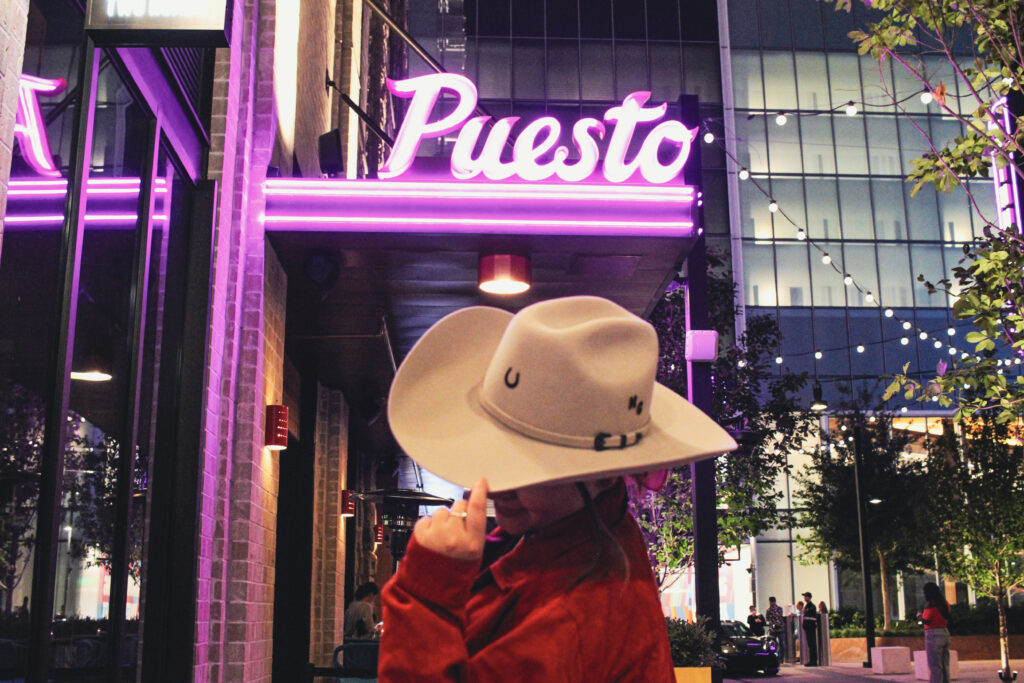 Custom cowgirl hat displayed beneath the Puesto restaurant sign at night in Nashville Yards, Nashville, TN.